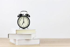 väckarklocka med böcker på trä skrivbord och vit bakgrund foto