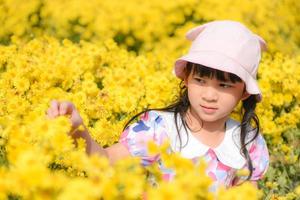 lite asiatiskt barn flicka ha kul med en glad på morgonen trädgård naturligt blommande gula blommor, söta flicka barn barn leker ute på ljusa dagen vacker blomma på våren utomhus foto