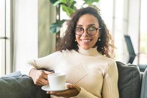 latinsk kvinna dricker kaffe på soffan hemma foto
