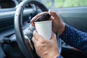 asiatisk dam som håller varm kaffekopp mat för dryck i bilen, farlig och riskerar en olycka. foto