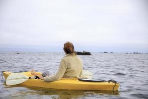 kvinna paddla kajak i en gul kajak runt stenar i havet foto