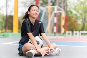 asiatisk unge flicka med en boll Sammanträde på utomhus- futsal sporter fält foto