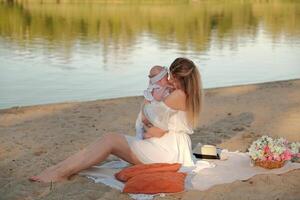 en skön flicka i en vit klänning med en nyfödd bebis är Sammanträde på de strand, på de sand. foto