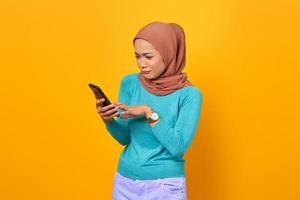 ledsen vacker ung asiatisk kvinna som använder smartphone isolerad på gul bakgrund foto