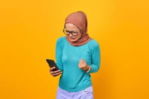 arg vacker ung asiatisk kvinna tittar på smartphone-skärmen isolerad på gul bakgrund