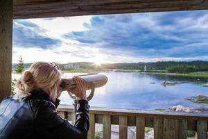 ung kvinna tittar på den fantastiska naturen genom en kikare i ett observationstorn foto