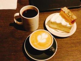 cappuccino med svart kaffe och brödsnacks med grädde på ett träbord foto