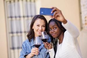 två kvinnor som gör en selfie med en smartphone medan de tar ett glas vin. foto