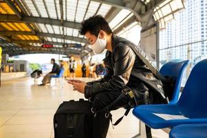 bild av asiatisk man som sitter och använder mobiltelefon på tågstationens plattform