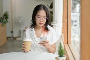 en kvinna är läsning meddelanden på henne smartphone medan Sammanträde på en tabell förbi de fönster i en Kafé. foto