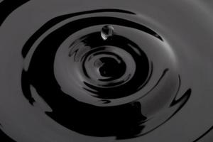 mörksvart transparent vattenvågsyta med stänkbubbla på svart vatten. foto