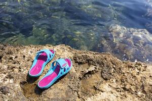 strandtofflor ligger på en sten nära det genomskinliga havet foto