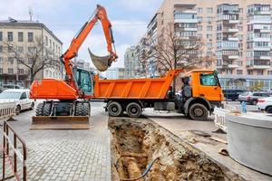 en grävmaskin och en lastbil vid reparation av en värmeledning på en stadsgata. foto