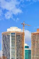 fragment av konstruktion av moderna bostadsskyskrapor med tornkran på en bakgrund av blå himmel.