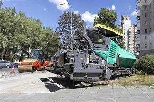 tung asfaltläggare och vägvibrerande rulltätning redo för reparationsvägar i en modern stad foto