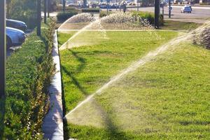 ett automatiskt sprinklersystem sprejar den gröna gräsmattan en ljus solig dag. foto