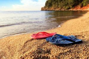 strandtofflor ligger på en sten nära det genomskinliga havet foto