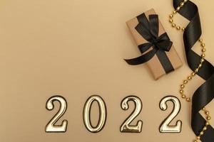 nyår 2022. ovanifrån nyårsmockup på beige bakgrund svart band, presentförpackning, gyllene siffror och flerfärgade gnistrar. layout av vykort foto