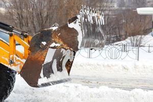 en traktor med hjälp av en stor glidande metallskopa rensar körbanan på en stadsgata från ett överflöd av snö. foto