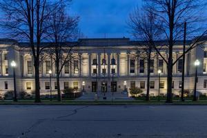 Kenosha County Courthouse, Wisconsin, upplyst på natten. höga majestätiska kala träd som kantar posten. stora trappsteg som leder till inträde. foto