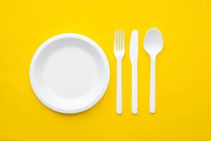 plast vit gaffel, kniv, sked och tallrik på gul bakgrund