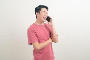 ung asiatisk man använder eller pratar smartphone och mobiltelefon med glada ansikte foto