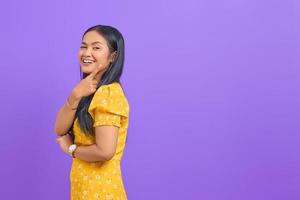 porträtt av leende ung asiatisk kvinna pekar finger på kopia utrymme på lila bakgrund foto