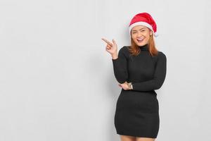 leende ung asiatisk kvinna i jultomten hatt pekar finger på kopia utrymme isolerade över vit bakgrund foto