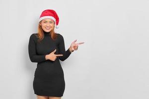leende ung asiatisk kvinna i jultomten hatt pekar finger på kopia utrymme isolerade över vit bakgrund foto