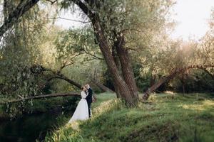 brudgummen och bruden går i skogen nära en smal flod foto