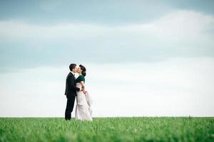 brudgummen i brun kostym och bruden i elfenbensfärgad klänning på ett grönt fält foto