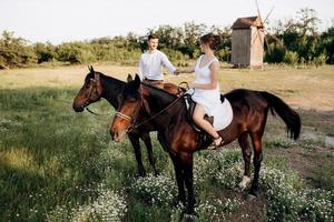 flicka i vit solklänning och en kille i vit skjorta på promenad med bruna hästar foto