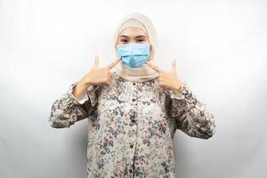 muslimsk kvinna som bär medicinsk mask med handen som pekar på masken, anti-coronavirusrörelse, anti covid-19-rörelse, hälsorörelse som använder mask, isolerad på vit bakgrund foto