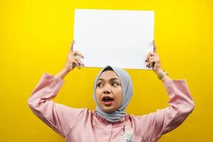 ganska ung muslimsk kvinna som håller tom tom banderoll, plakat, vit tavla, tom skylttavla, vit reklamtavla, presenterar något i kopieringsutrymme, marknadsföring