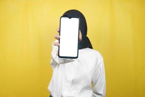 muslimsk kvinna med händer som håller smartphone, marknadsför app, främjar något, isolerad på gul bakgrund, reklamkoncept foto