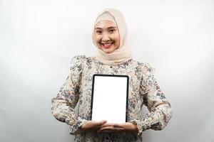 vacker ung asiatisk muslimsk kvinna som ler, upprymd och glad håller surfplatta med vit eller tom skärm, marknadsför app, marknadsför produkt, presenterar något, isolerad på vit bakgrund