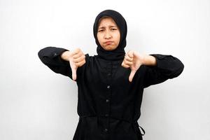 vacker och glad ung asiatisk muslimsk kvinna med ogillar hand, tummen ner, isolerad på vit bakgrund foto