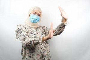 muslimsk kvinna som bär medicinsk mask med hand som avvisar något, hand som stoppar något, hand som ogillar något, isolerad på vit bakgrund foto
