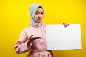 ganska ung muslimsk kvinna som tänker, hand som håller tom tom banderoll, plakat, vit tavla, tom skylttavla, vit reklamtavla, presenterar något i kopieringsutrymmet, marknadsföring foto