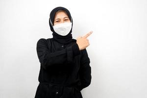 muslimsk kvinna som bär vit mask, med handen som pekar på tomt utrymme som presenterar något, isolerad på vit bakgrund foto