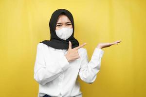 muslimsk kvinna som ler självsäkert med händer som pekar på tomt utrymme, presenterar något, presenterar produkt, isolerad på gul bakgrund foto