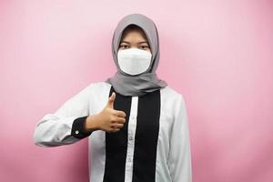 muslimsk kvinna som bär vita masker, anti-coronavirusrörelse, anti covid-19-rörelse, hälsorörelse som använder masker, med händer som visar ok-tecken, bra arbete, framgång, seger, isolerad på rosa bakgrund