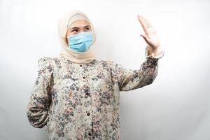 muslimsk kvinna som bär medicinsk mask med hand som avvisar något, hand som stoppar något, hand som ogillar något, isolerad på vit bakgrund foto