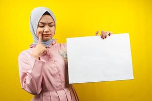ganska ung muslimsk kvinna som tänker, hand som håller tom tom banderoll, plakat, vit tavla, tom skylttavla, vit reklamtavla, presenterar något i kopieringsutrymmet, marknadsföring foto