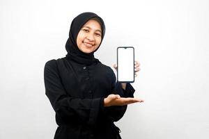 vacker ung asiatisk muslimsk kvinna som ler självsäkert och upprymt med händer som håller smartphone, marknadsför app, främjar något, isolerad på vit bakgrund, reklamkoncept foto