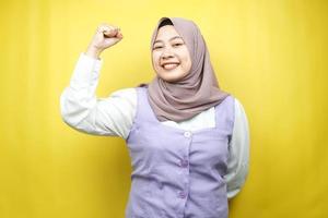vacker asiatisk ung muslimsk kvinna med upphöjda muskler, styrka tecken armar, isolerad på gul bakgrund foto
