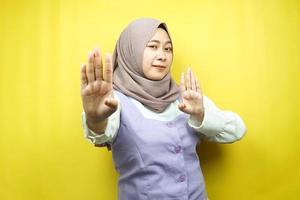 vacker asiatisk ung muslimsk kvinna med stoppskylt hand, avvisa tecken hand, förbudsskylt hand, närma sig inte handen, håll dig borta tecken hand, rör inte tecken hand, isolerad på gul bakgrund foto