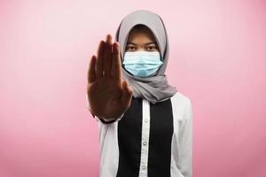 muslimsk kvinna bär medicinsk mask, med stoppskylt hand, avslagstecken hand, håll inte avstånd tecken hand, närma sig inte hand tecken, isolerad på rosa bakgrund foto