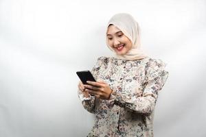 vacker ung asiatisk muslimsk kvinna som ler tryggt och håller smartphone isolerad på vit bakgrund, reklamkoncept