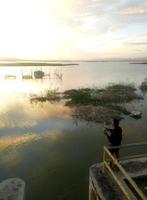 man fiskare som fiskar med ett spinnspö i sjön på eftermiddagen. solnedgång på limboto sjön, Indonesien foto